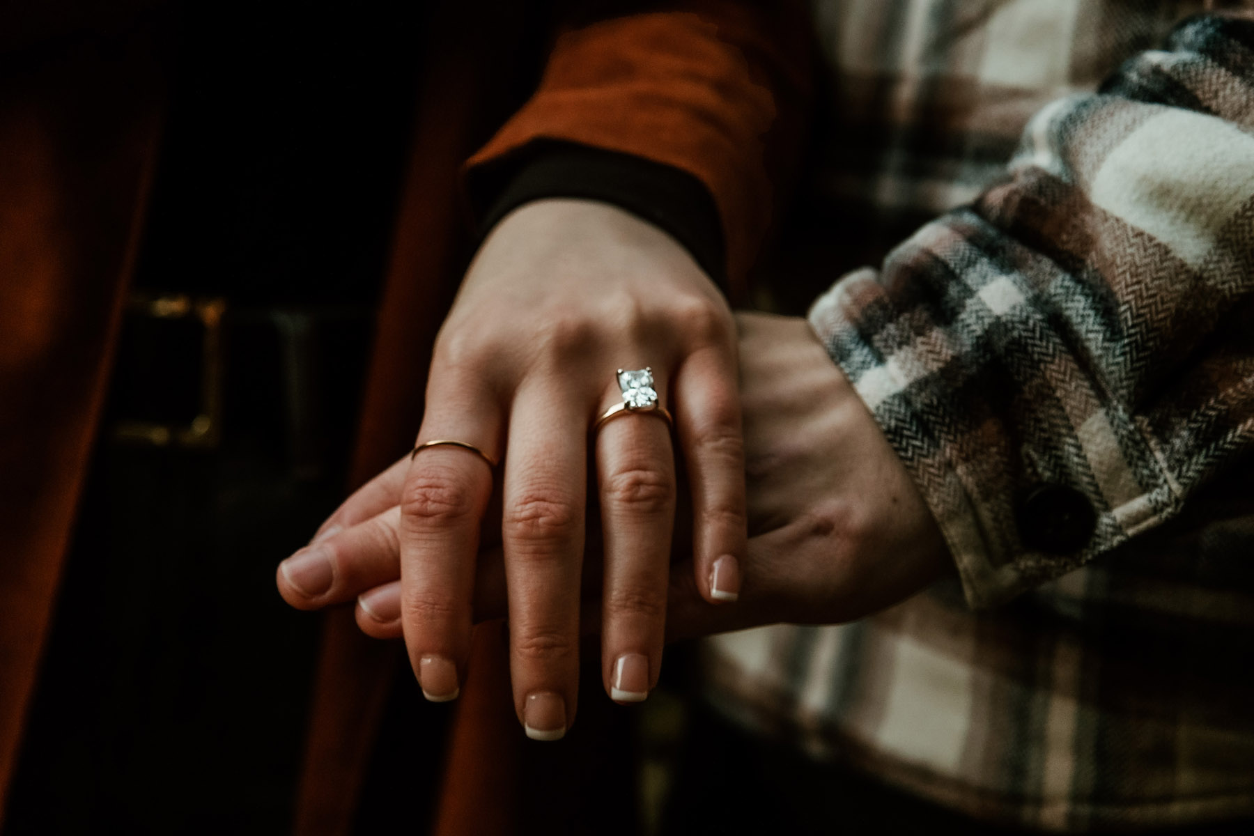 Close-up of a couple holding hands, showcasing an engagement ring after a proposal